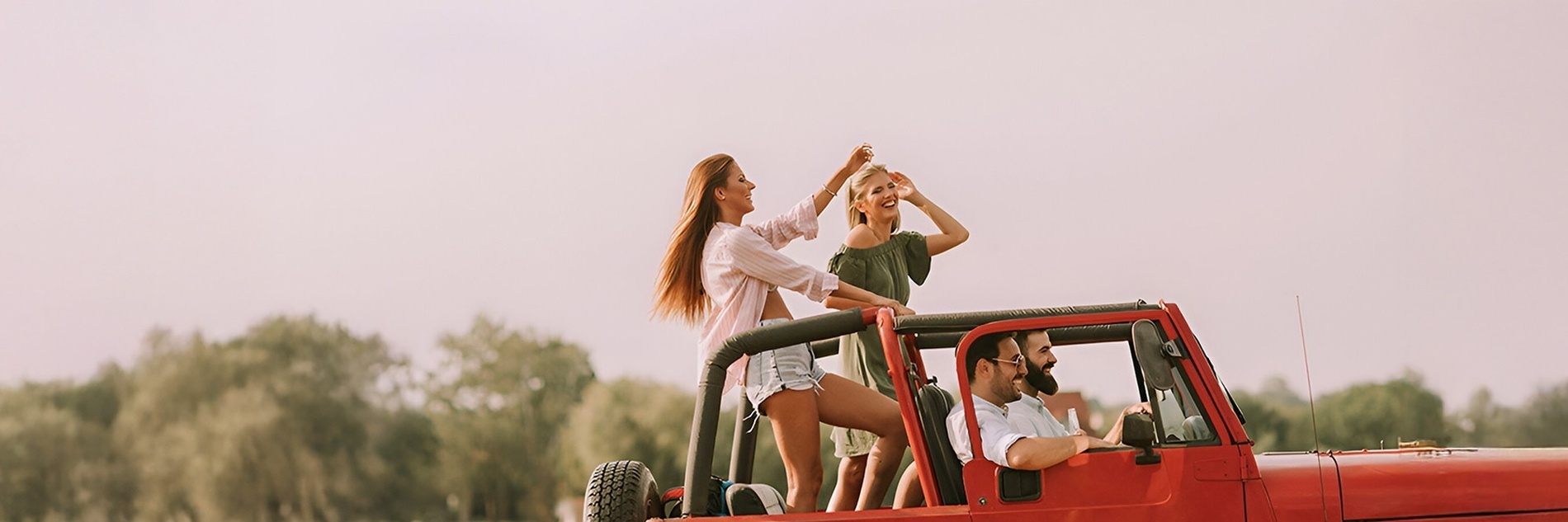 un homme conduit une jeep rouge avec trois personnes assises sur le toit
