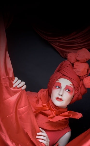 una mujer con maquillaje rojo y un turbante rojo sostiene una cortina roja