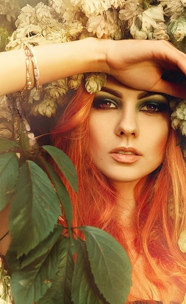 una mujer con cabello rojo y ojos verdes está rodeada de hojas y flores