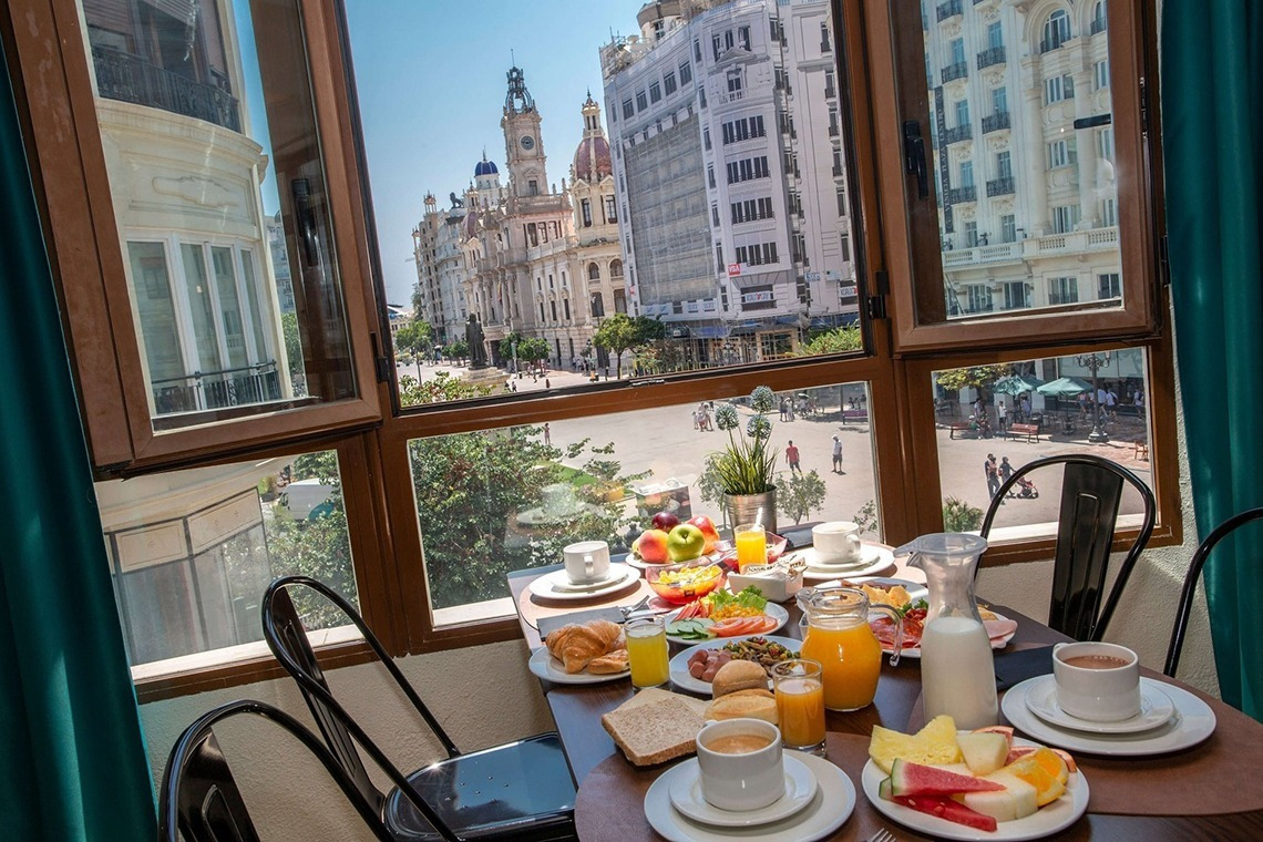 a table with plates of food and drinks in front of a window with a view of a city