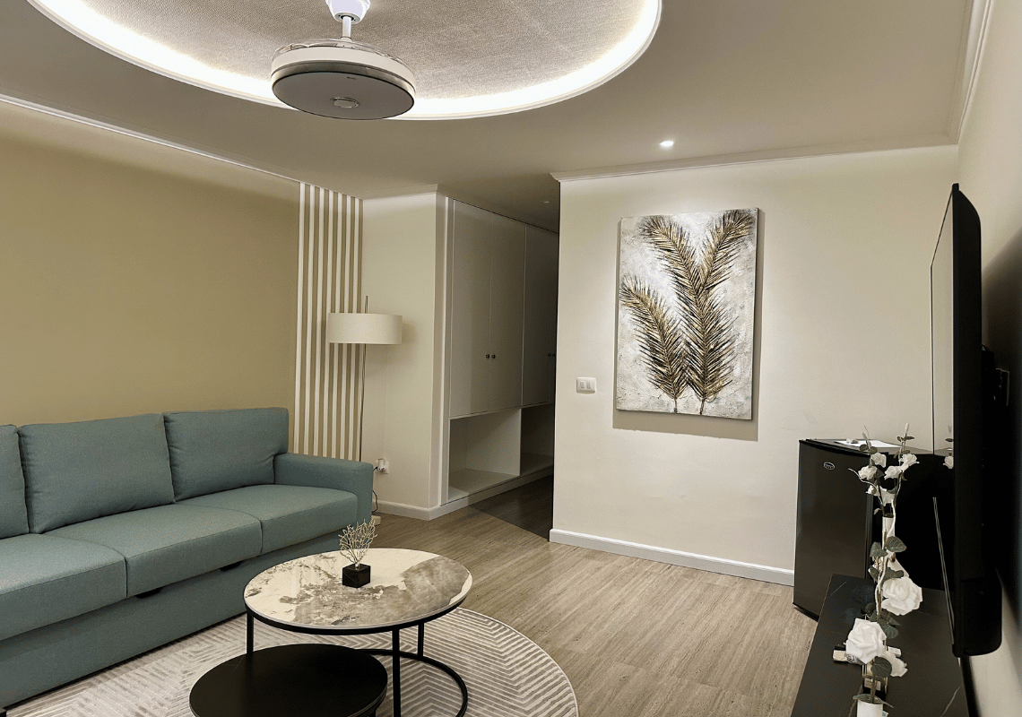 Soggiorno moderno con divano blu, tavolini, quadro di foglie dorate e minifrigo. Casual: Eden Bayahibe perfetto per il relax.