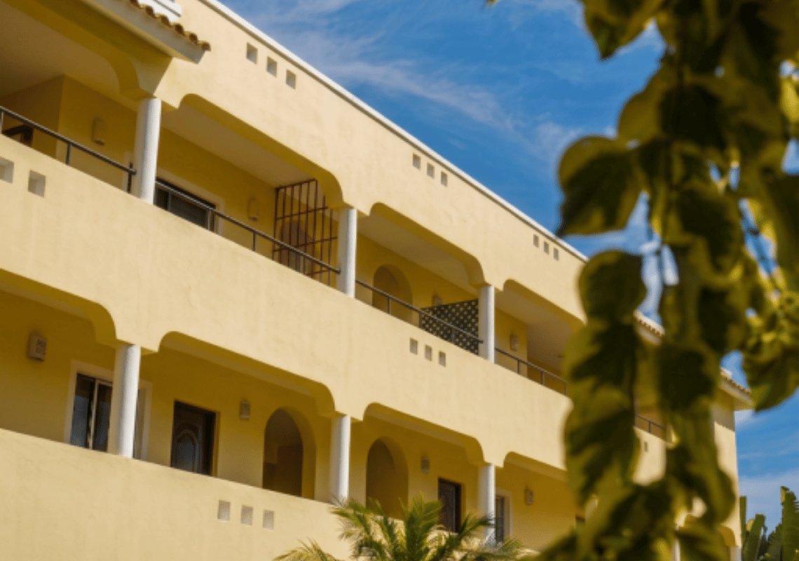 Hotel giallo con balconi e vista sul cielo azzurro con alberi in primo piano Casual: Eden Bayahibe