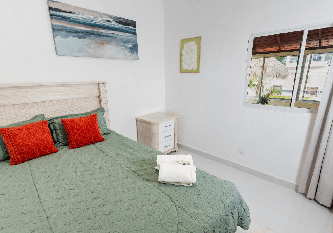 Cama acogedora con cojines naranjas y vista al exterior desde la ventana de la habitación Casual: Green Village Bayahibe.