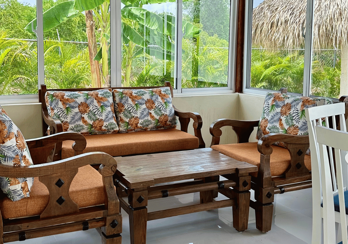 Salon extérieur avec vue tropicale sur un hôtel. Meubles en bois et coussins décorés de Casual: Green Village Bayahibe.