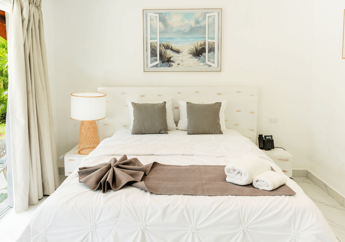 Cama doble cómoda con Casual: Green Village Bayahibe, almohadas grises y pintura de playa en habitación luminosa.