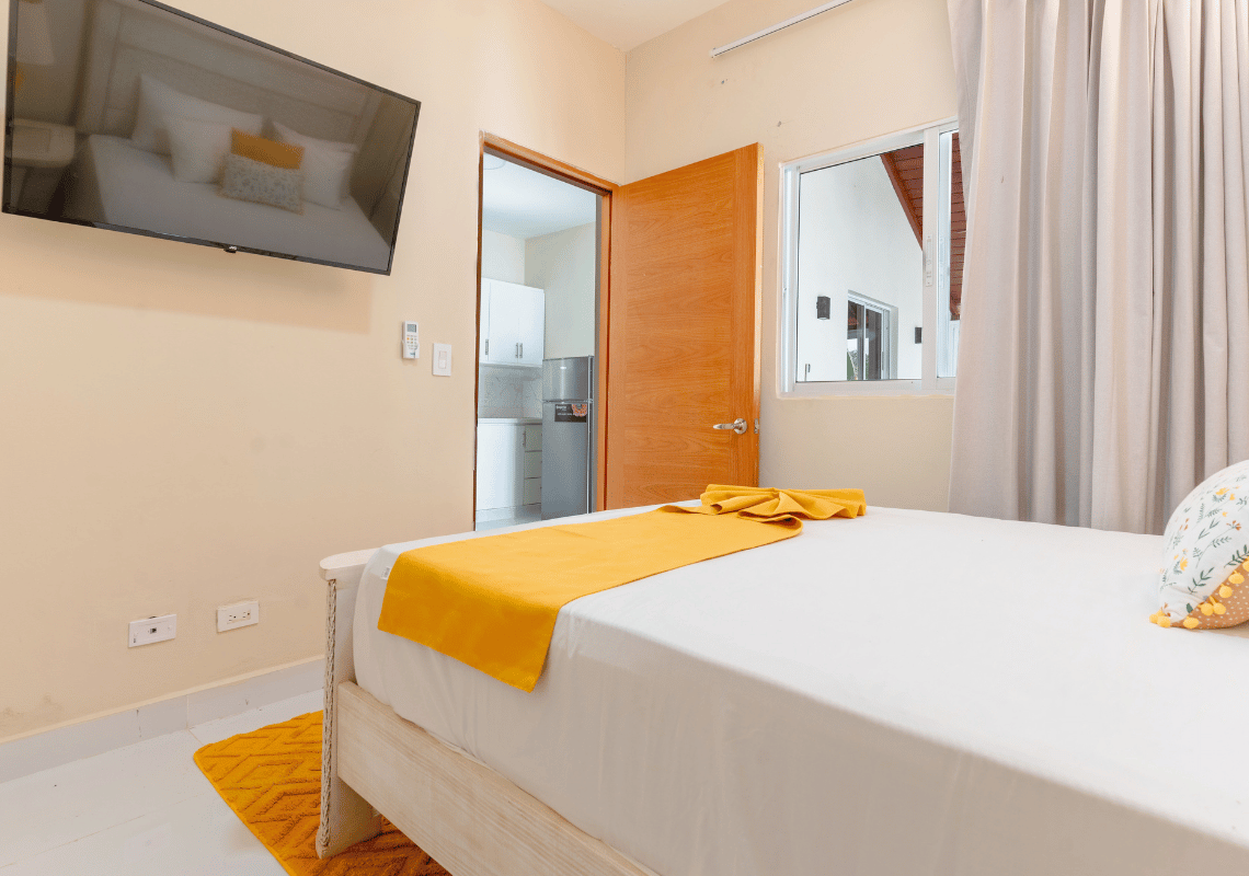 Cama con acento amarillo en dormitorio de hotel. Casual: Green Village Bayahibe.