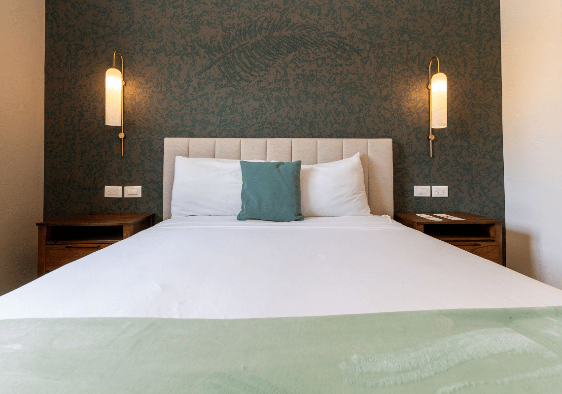 Cama confortable con almohadas blancas y cojín verde, mesitas de noche y lámparas de pared. Casual: Green Village Bayahibe