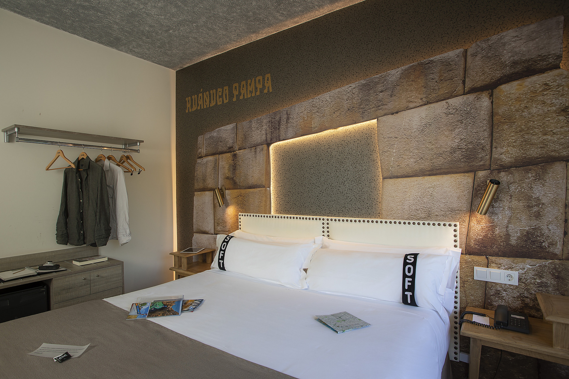 Habitación de hotel moderna con textiles 'Casual: Inca Porto' en la cama y un diseño de pared de piedra.