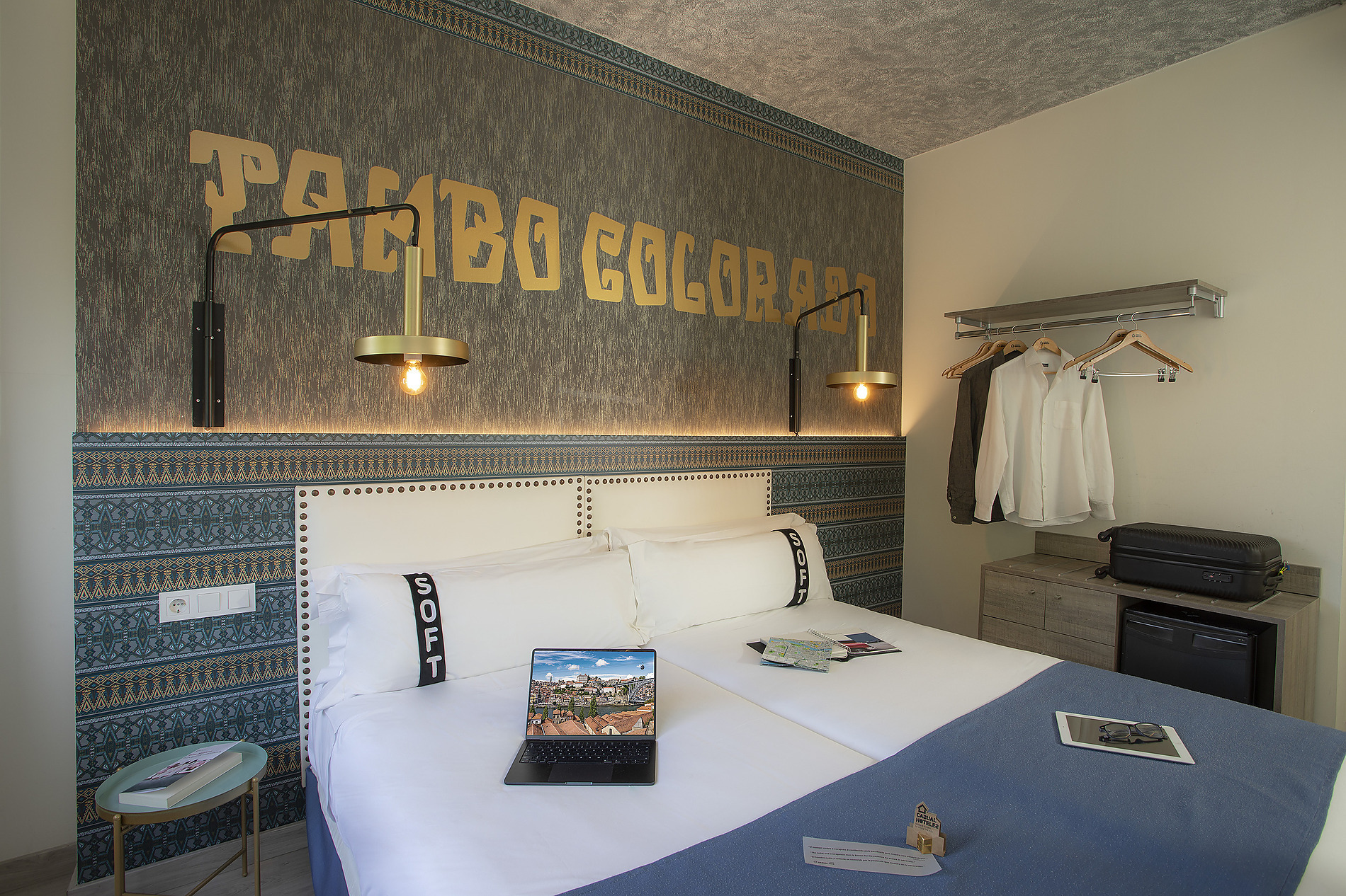 Cama cómoda en habitación de hotel con Casual: Inca Porto, luces y ropa en perchas.