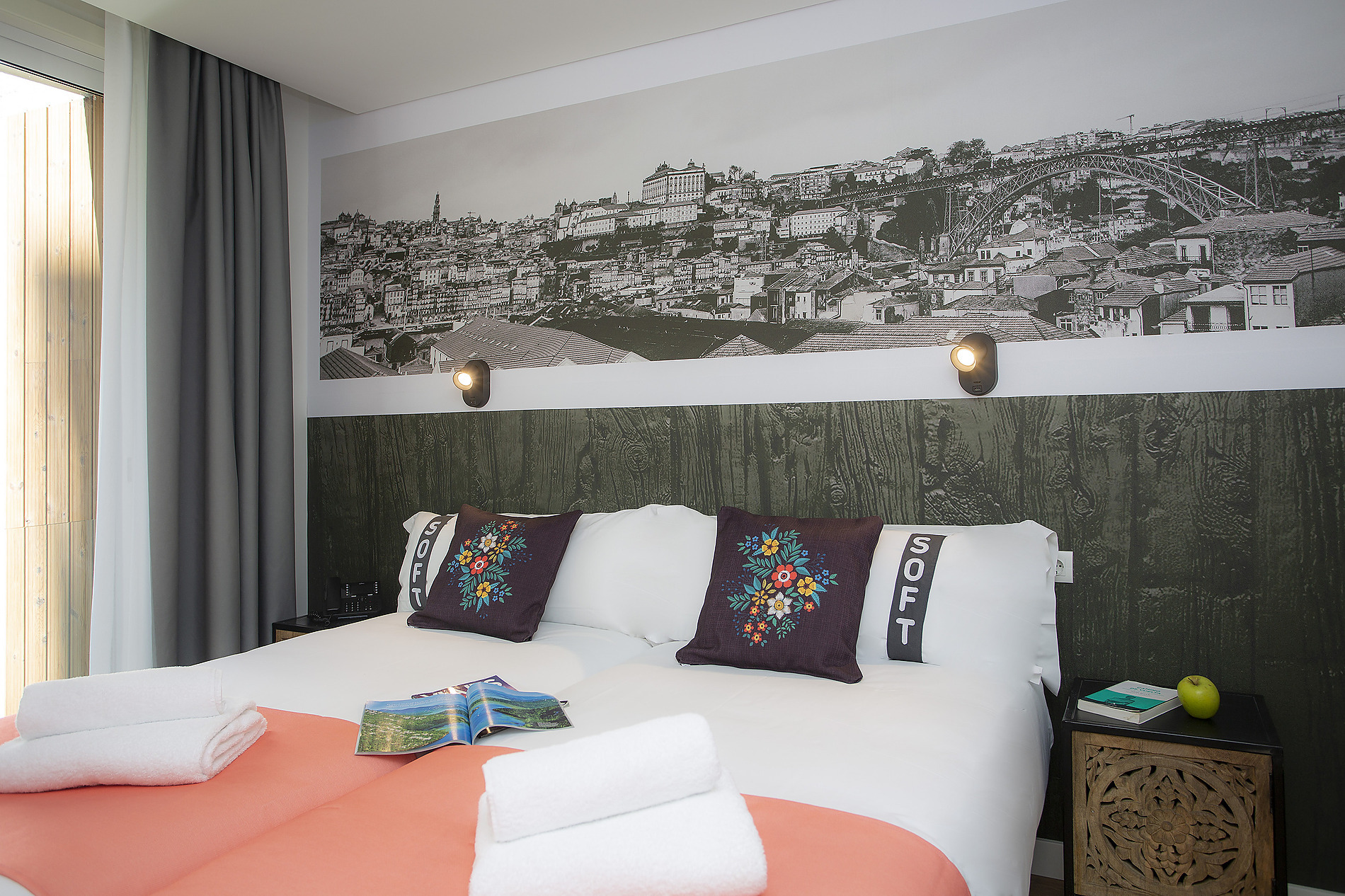 Cama doble con almohadas decorativas, un libro y toallas apiladas, un detalle de 'SOFT' y un mural de ciudad, ideal para tu estancia Casual: Raizes Porto.