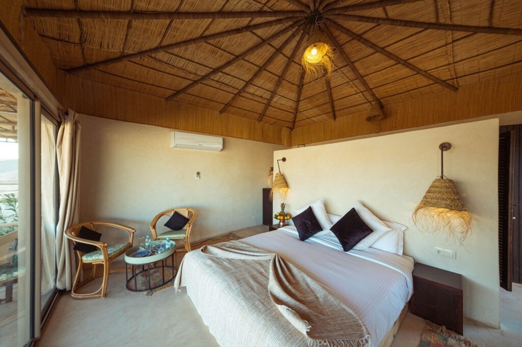 una habitación con una cama y dos sillas y un techo de paja