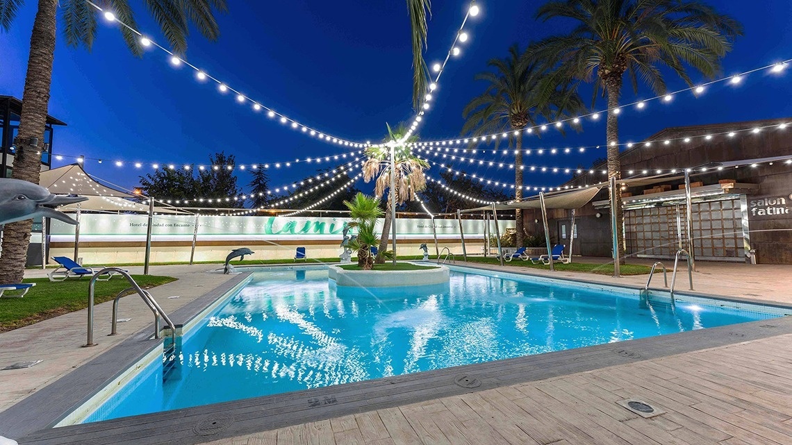 a large swimming pool is surrounded by palm trees and string lights