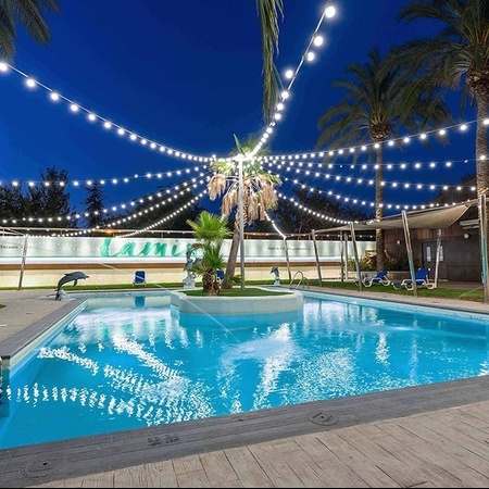 a large swimming pool is surrounded by palm trees and string lights