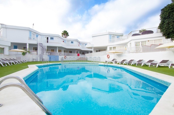 una piscina rodeada de sillas y sombrillas en un complejo de apartamentos