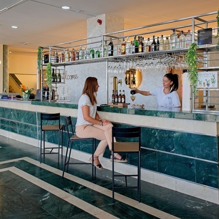 una mujer se sienta en una silla en un bar mientras una camarera sirve bebidas