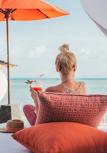 una mujer está sentada en una cama en la playa con un cóctel en la mano .