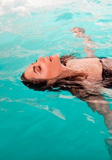 una mujer está flotando en el agua en una piscina con los ojos cerrados .