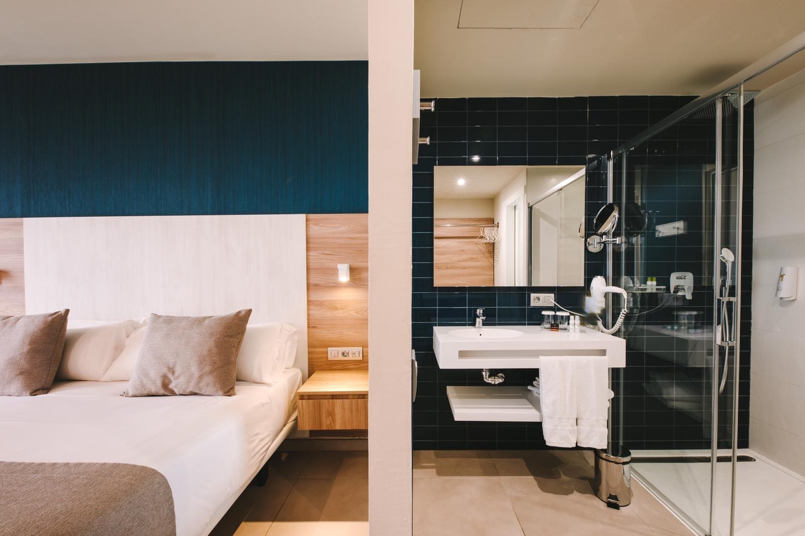 Modern hotel room and bathroom at Club Maspalomas with comfortable bed and sleek shower.