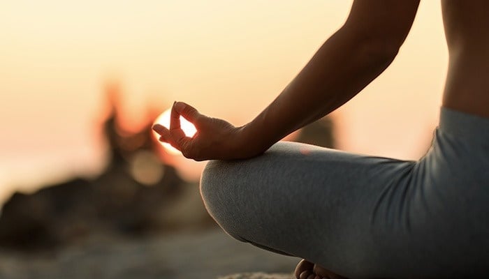 una mujer está sentada en una pose de yoga con el sol brillando a través de sus dedos
