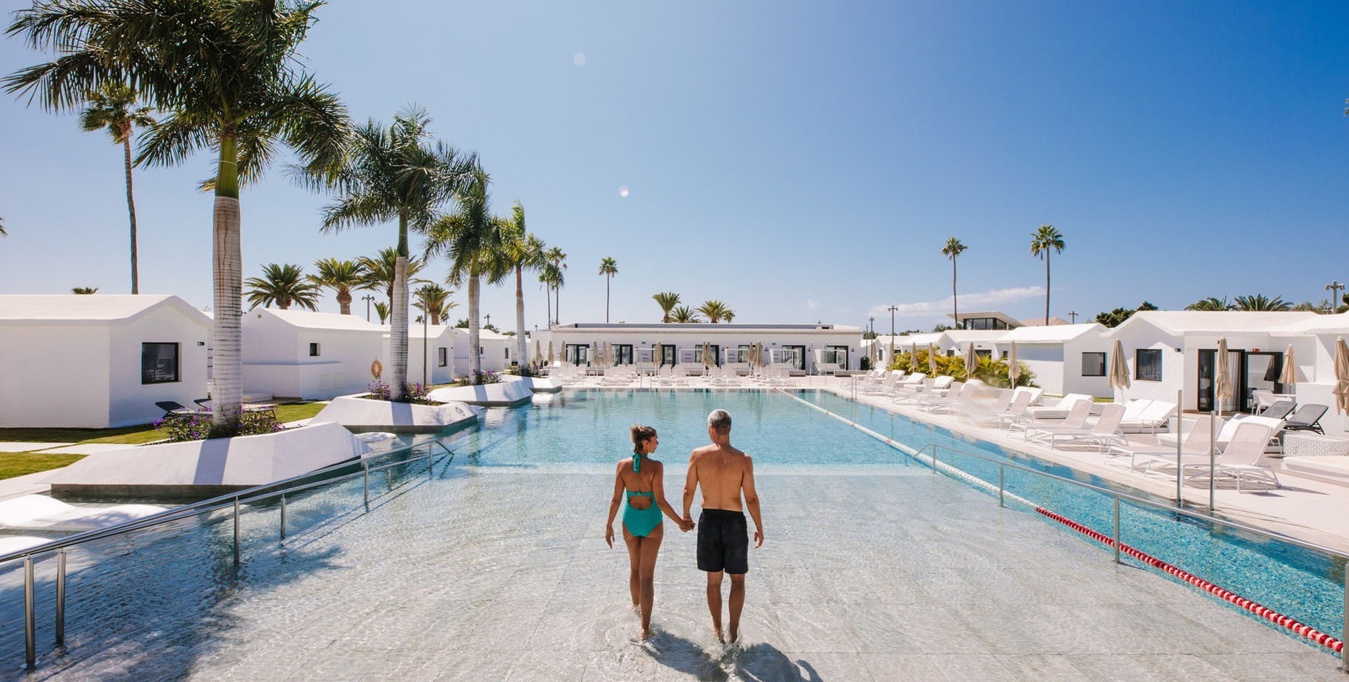 un hombre y una mujer caminan por una piscina en un resort