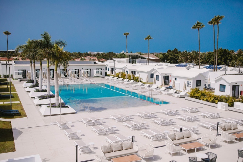 una gran piscina rodeada de muebles blancos y palmeras