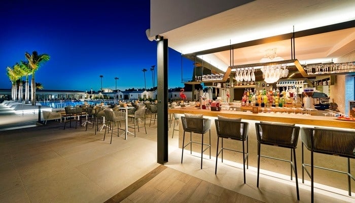 un bar con sillas y mesas y una piscina en el fondo