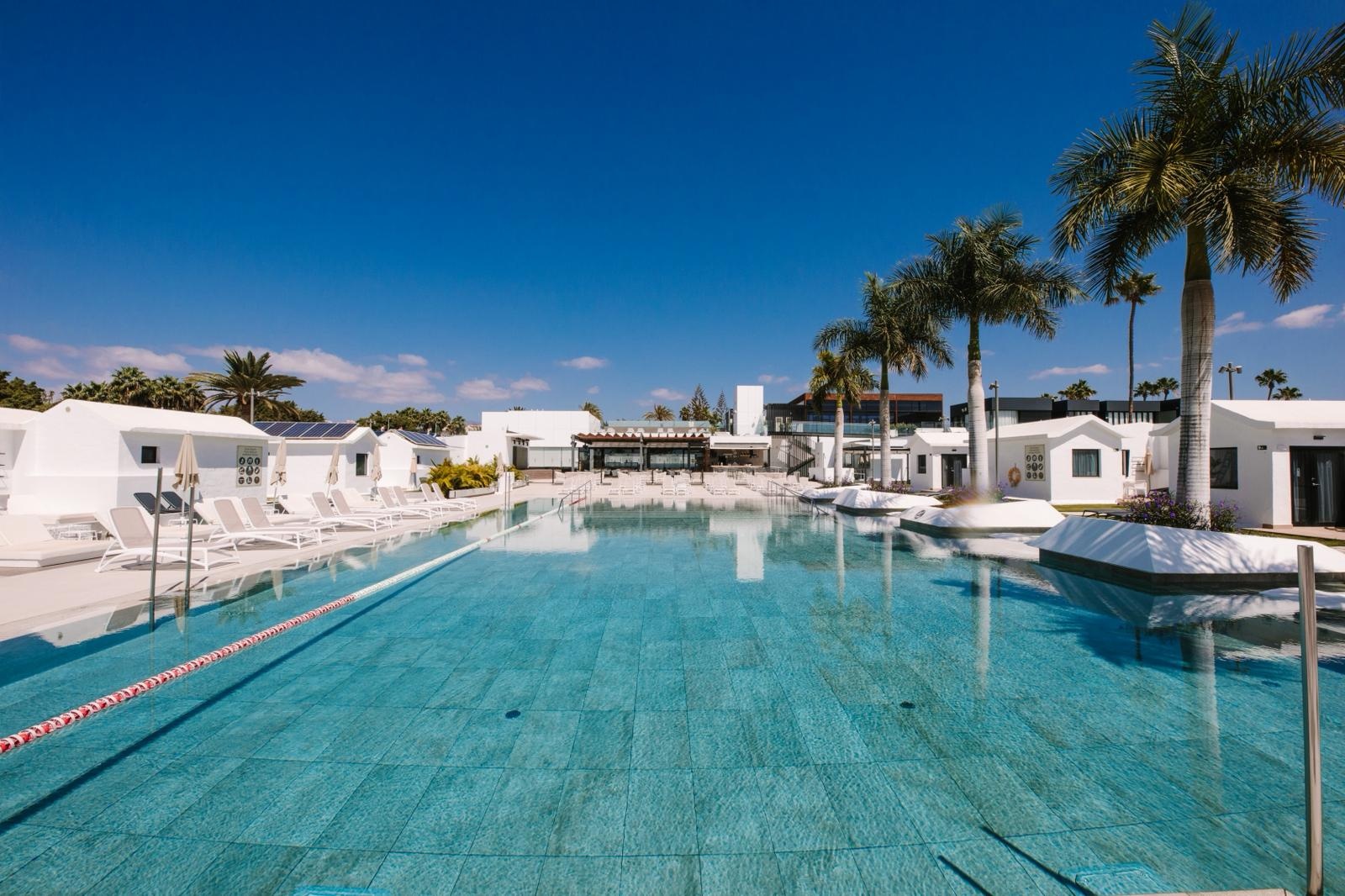 Club Maspalomas: weiße Bungalows und Poolbereich mit Palmen.