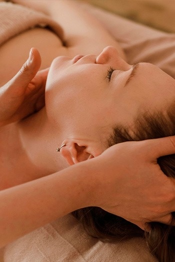 Una persona con los ojos cerrados recibe un masaje en la cabeza y el cuello, evocando una sensación de relajación y bienestar.