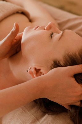 Una persona con los ojos cerrados recibe un masaje en la cabeza y el cuello, evocando una sensación de relajación y bienestar.