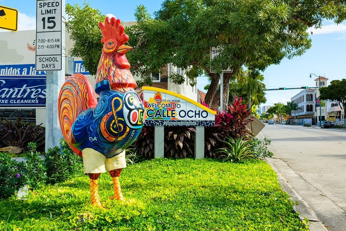 a statue of a rooster in front of a sign that says welcome to or calle ocho