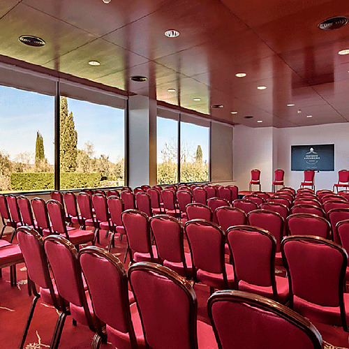 Sala de conferencias elegante en Convento do Espinheiro, con sillas rojas y vistas al jardín.
