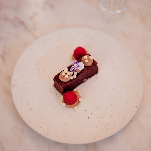 un plato blanco con un pastel de chocolate y frambuesas encima