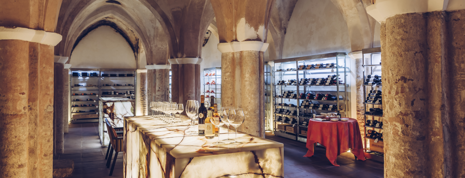 uma mesa com taças e garrafas de vinho e uma toalha vermelha