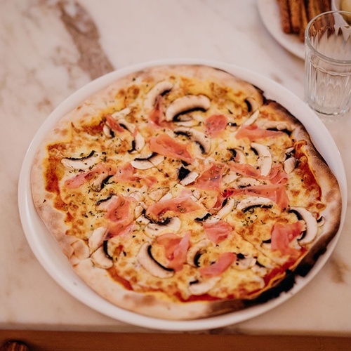 una pizza con champiñones y jamón en un plato blanco