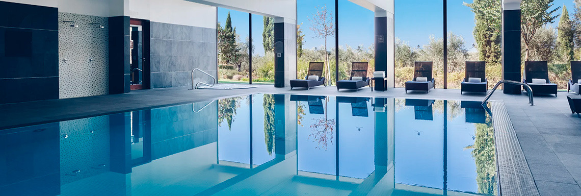 Piscina interior moderna com espreguiçadeiras e vista para o spa | Convento do Espinheiro, Historic Hotel & Spa.