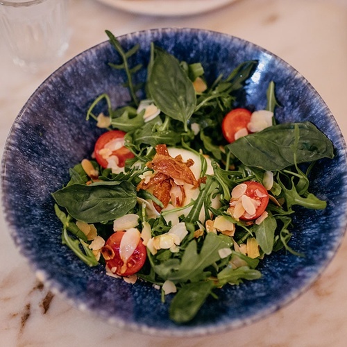 un tazón azul lleno de una ensalada con tomates y albahaca