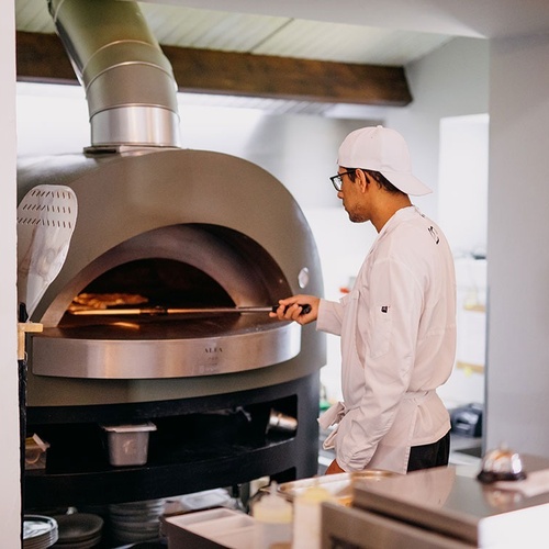un chef prepara una pizza en un horno de pizza de acero inoxidable