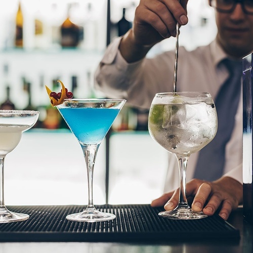 un barman vierte un cóctel azul en una copa de martini