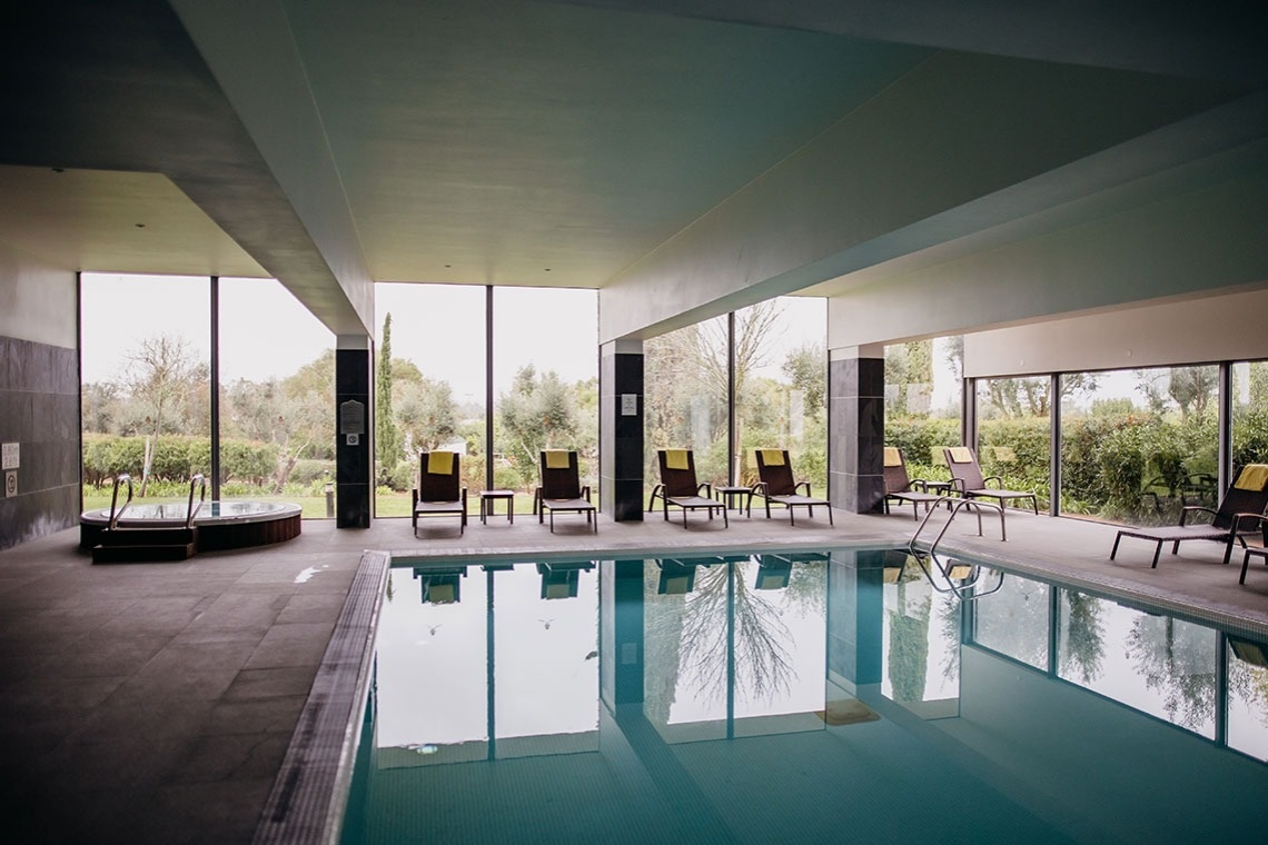 Piscina interior con jacuzzi en Convento do Espinheiro, rodeada de tumbonas y vistas al jardín.