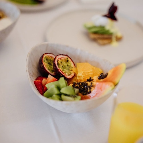 un tazón de frutas está sobre una mesa junto a un vaso de jugo de naranja