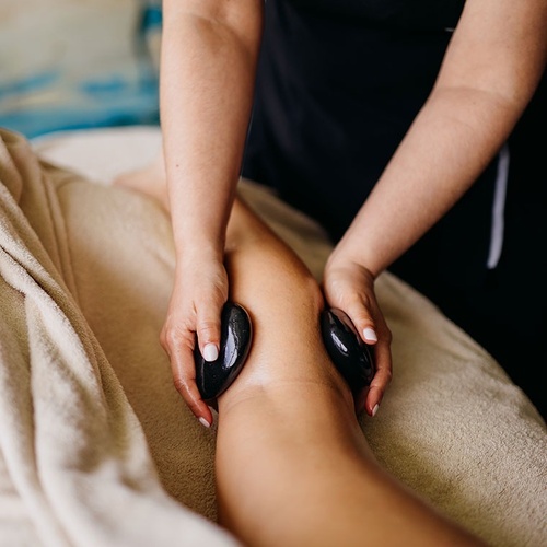 una mujer recibe un masaje con piedras negras en la pierna