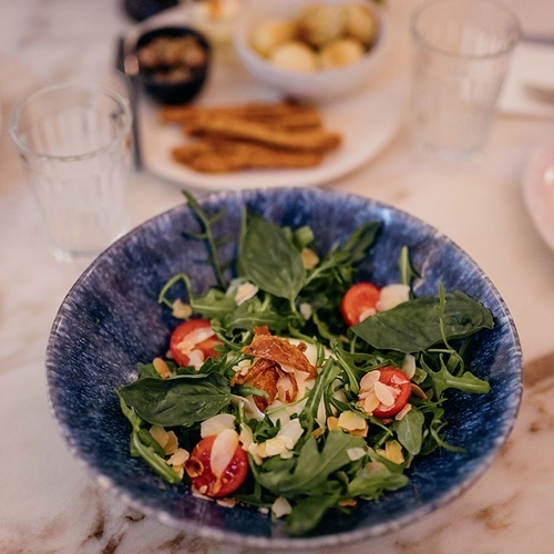 un plato azul lleno de ensalada con tomates y albahaca