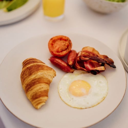 un plato de desayuno con huevos fritos tomates bacon y un cruasán