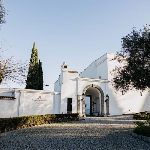 un edificio blanco con una puerta arqueada está rodeado de árboles y arbustos