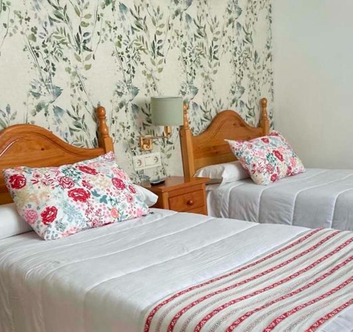 two beds in a hotel room with floral wallpaper on the wall