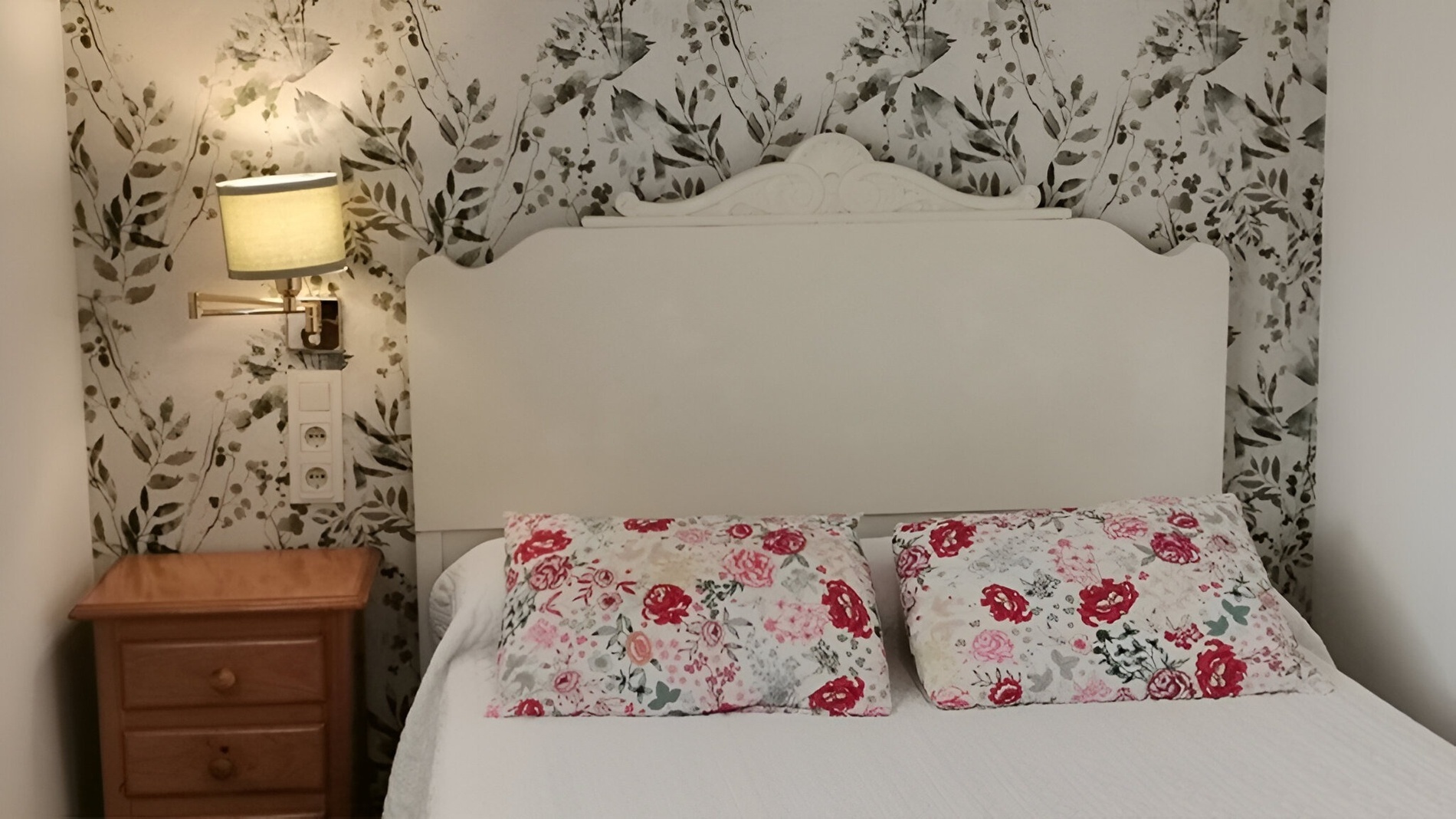 a bedroom with a white headboard and floral wallpaper