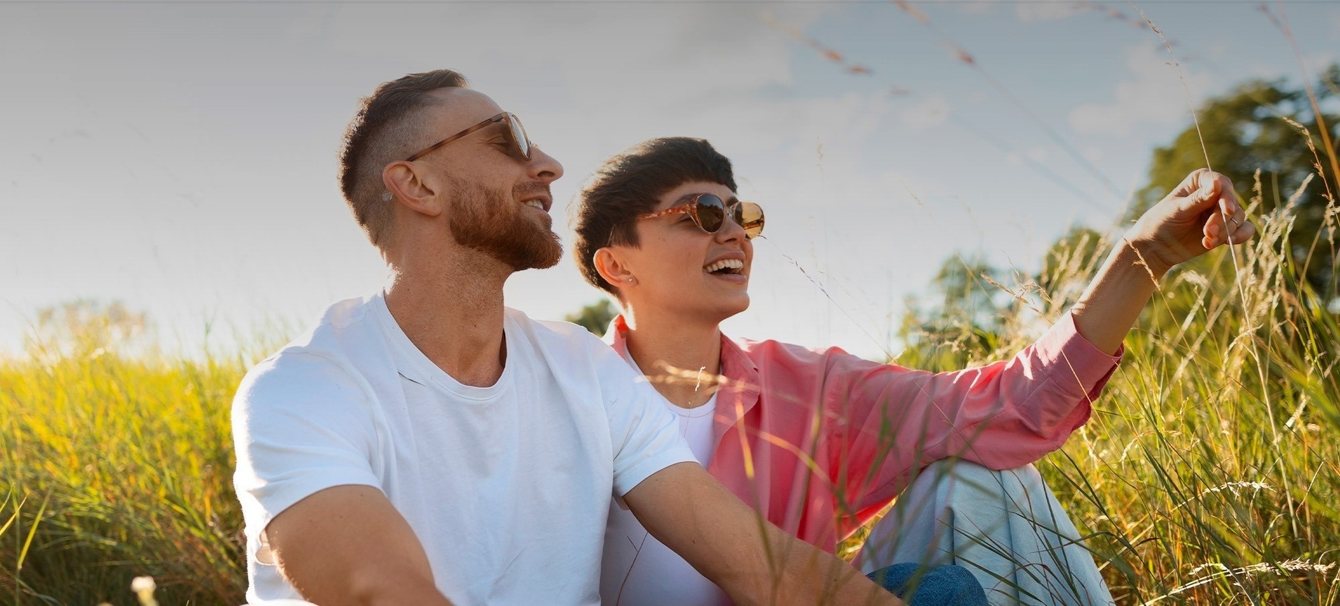 a man and woman wearing sunglasses sit in a field of tall grass