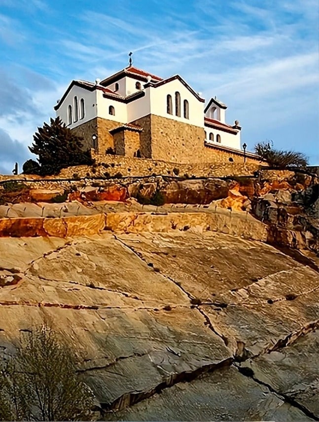 una iglesia blanca y de piedra está encima de una colina rocosa