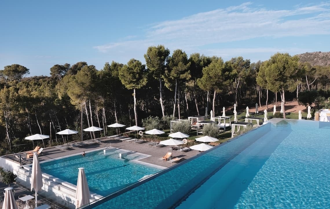 ein großer Pool mit vielen Sonnenschirmen und Bäumen im Hintergrund