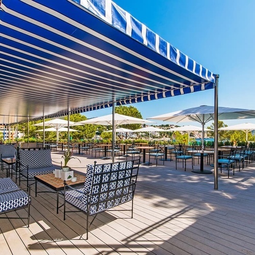 eine Terrasse mit blau-weißem Zelt und vielen Stühlen und Tischen